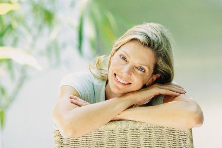 Smiling Woman Leaning Against Wicker Chair --- Image by © Image Source/Corbis